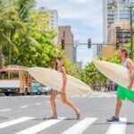 Find out the best Oahu travel tips recommended by top Hawaii blog Hawaii Travel Spot! Image of a man and woman holding surfboards in Waikiki