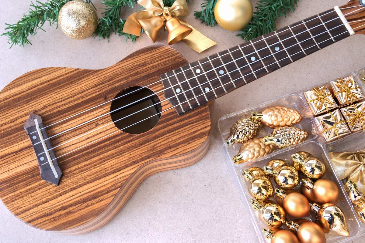 Check out this list of the best Hawaiian Christmas music recommended by top Hawaii blog Hawaii Travel Spot! Image of The ukulele on the wooden table with christmas golden decoration set, ukulele is a gift from the christmas day