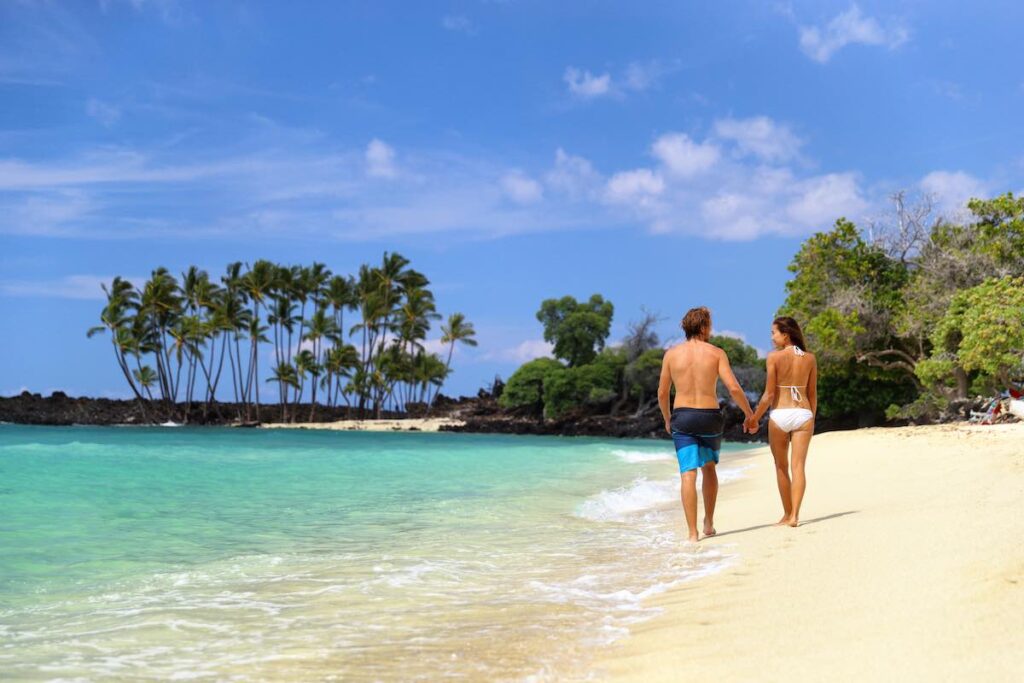 Check out these amazing Big Island Hawaii honeymoon resorts recommended by top Hawaii blog Hawaii Travel Spot. Image of a couple holding hands on the beach