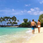 Check out these amazing Big Island Hawaii honeymoon resorts recommended by top Hawaii blog Hawaii Travel Spot. Image of a couple holding hands on the beach