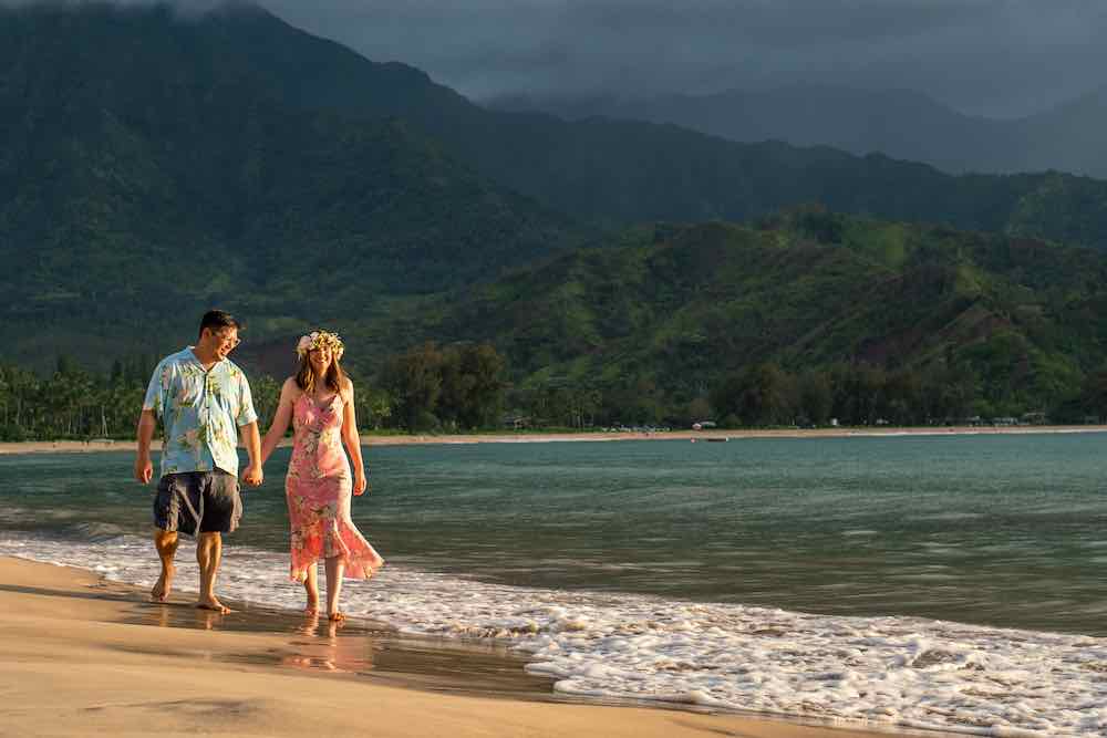 Image of a couple wearing Aloha wear walking along Hanalei Bay on Kauai