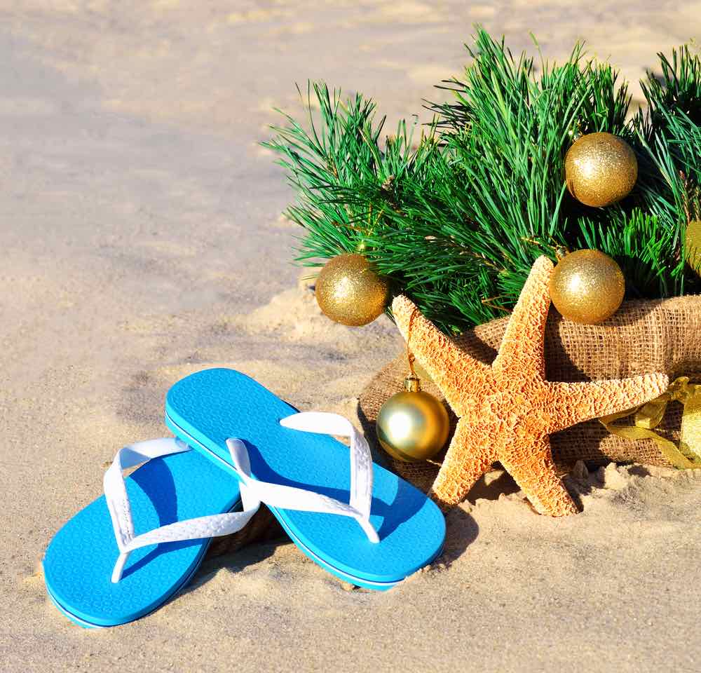 Find out what to pack for winter in Hawaii. Christmas tree with christmas balls, slippers and starfish on the sand on beach