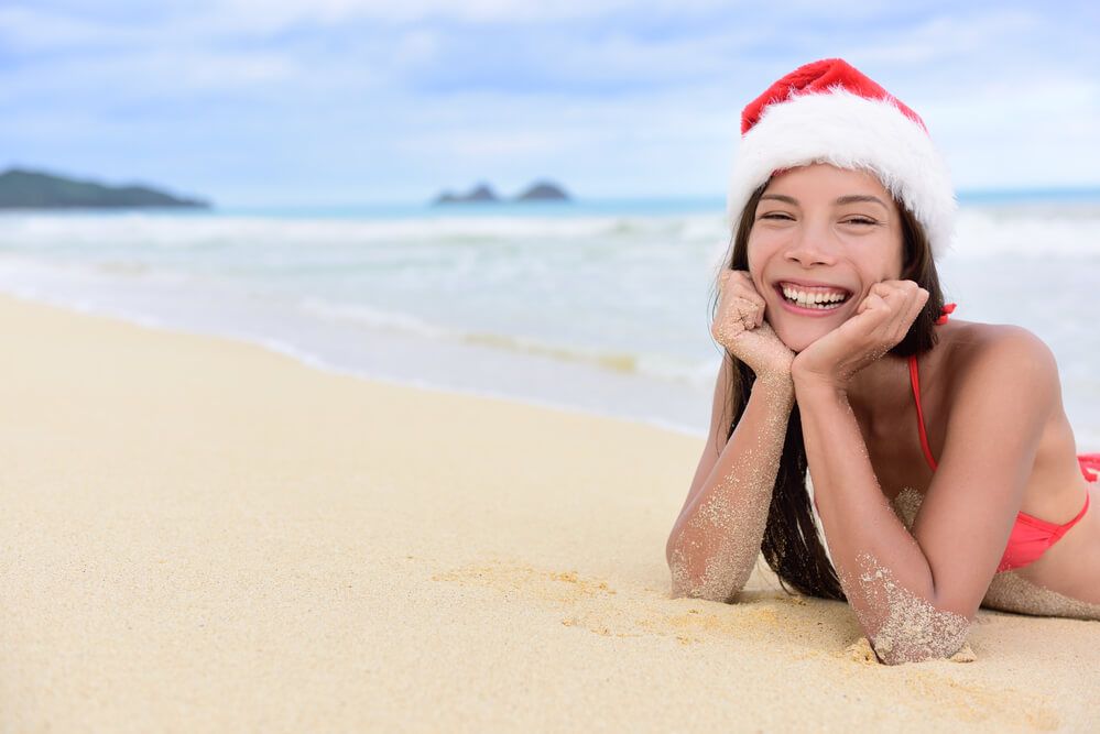 Oahu Christmas weather is usually in the 80s. Image of a woman wearing a red bikini and Santa hat on a beach on Oahu