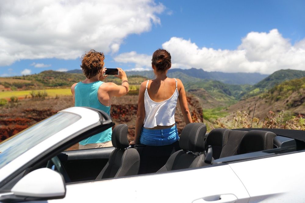 Road trip car people taking phone pictures of nature landscape on summer travel vacation. Tourists couple taking photos on Hawaii Kauai island, with smartphone camera app.