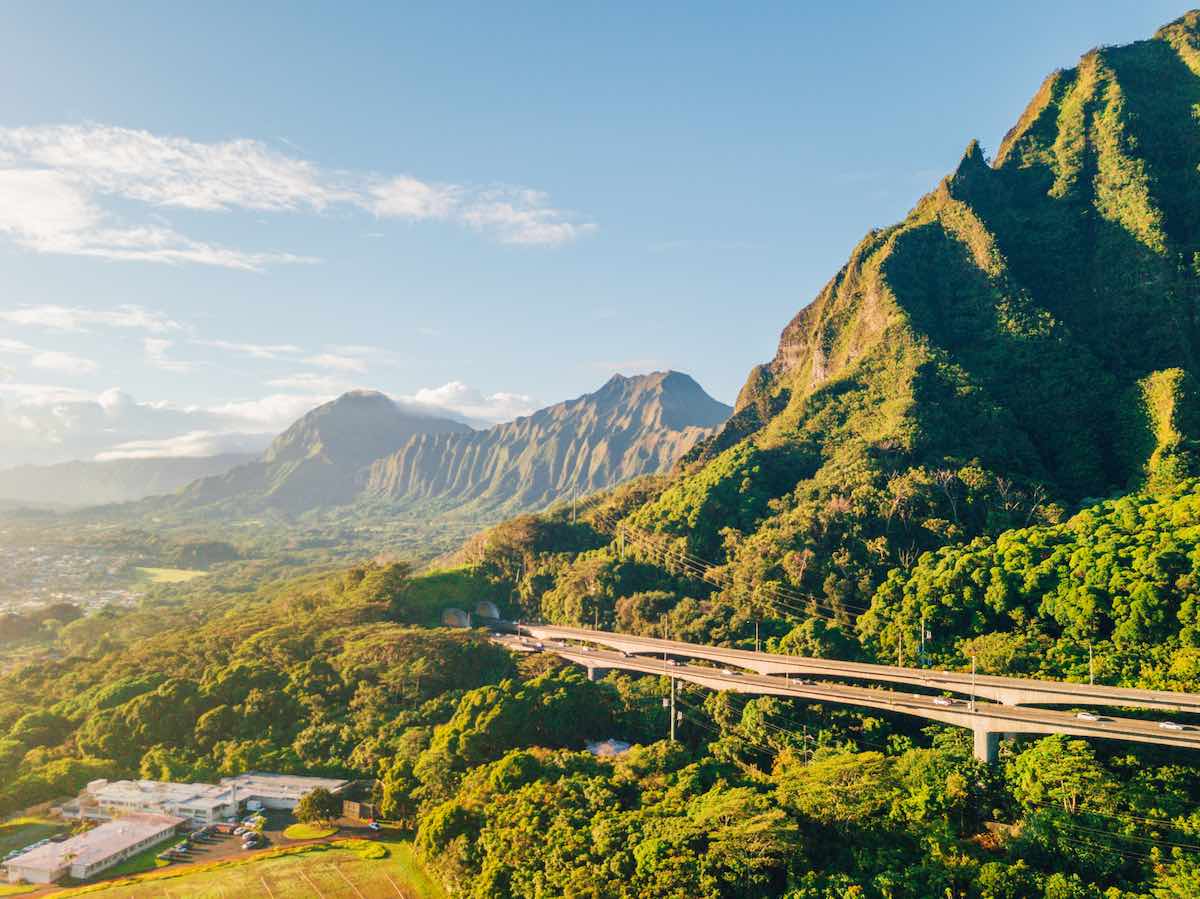 Check out the best things to do in Kaneohe Oahu recommended by top Hawaii blog Hawaii Travel Spot! Image of a highway going around tropical mountains as seen from Hoomaluhia Botanical Garden.