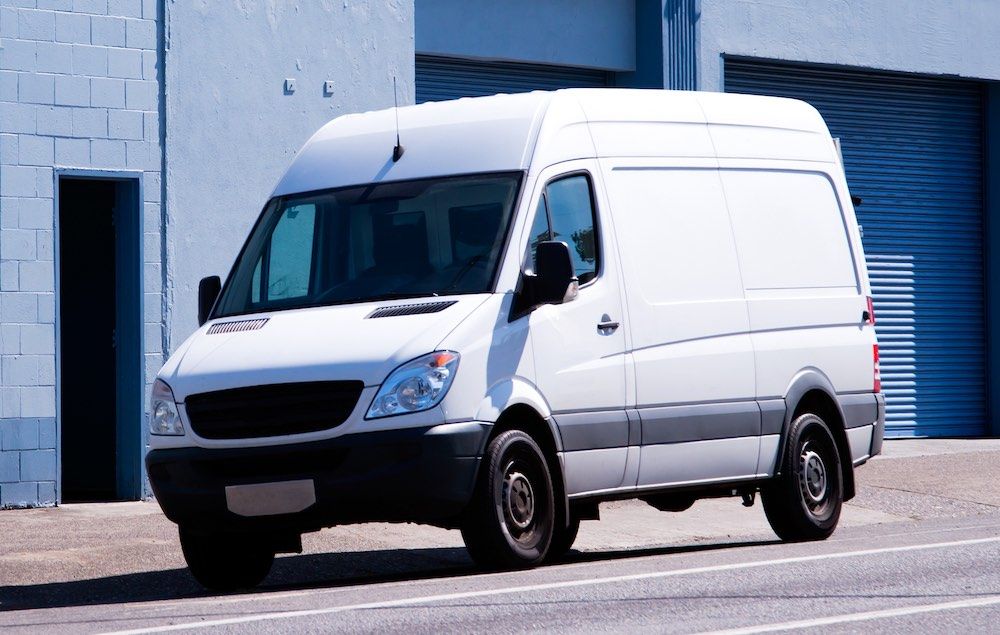 Image Small compact white minivan for commercial transportation and small business - convenient and practical vehicle standing on urban city street with warehouse buildings