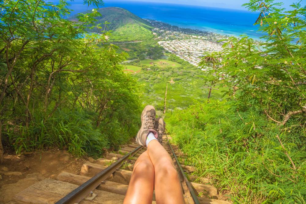 Legs of traveler sitting at the beginning of 1048 steps of popular Hawaiian hiking, koko head stairs hike. Hiking boots on stairway of scenic trekking in Oahu, Hawaii, United States.