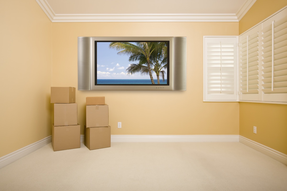 Find out everything you need to know about moving to Hawaii from the Mainland by top Hawaii blog Hawaii Travel Spot! Image of Flat Panel Television on Wall with Tropical Scene in Empty Room with Boxes.