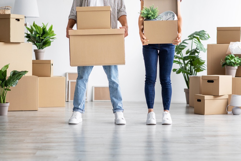 European young wife and husband in casual hold cardboard boxes with belongings, moving to new home, unrecognizable, empty space. Relocation together, credit and mortgage, buying own first real estate