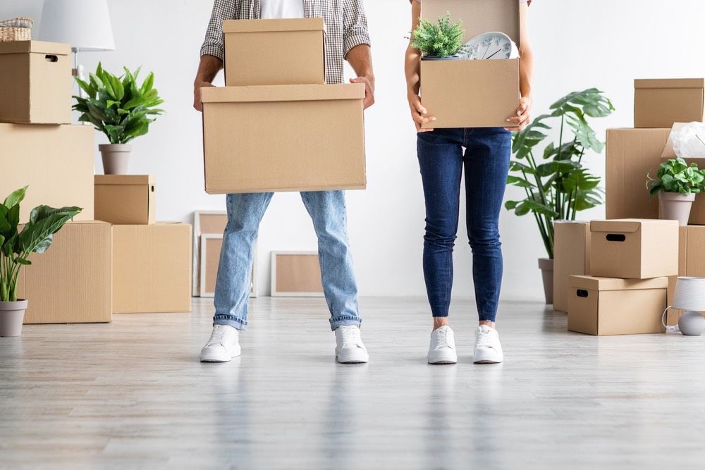 European young wife and husband in casual hold cardboard boxes with belongings, moving to new home, unrecognizable, empty space. Relocation together, credit and mortgage, buying own first real estate