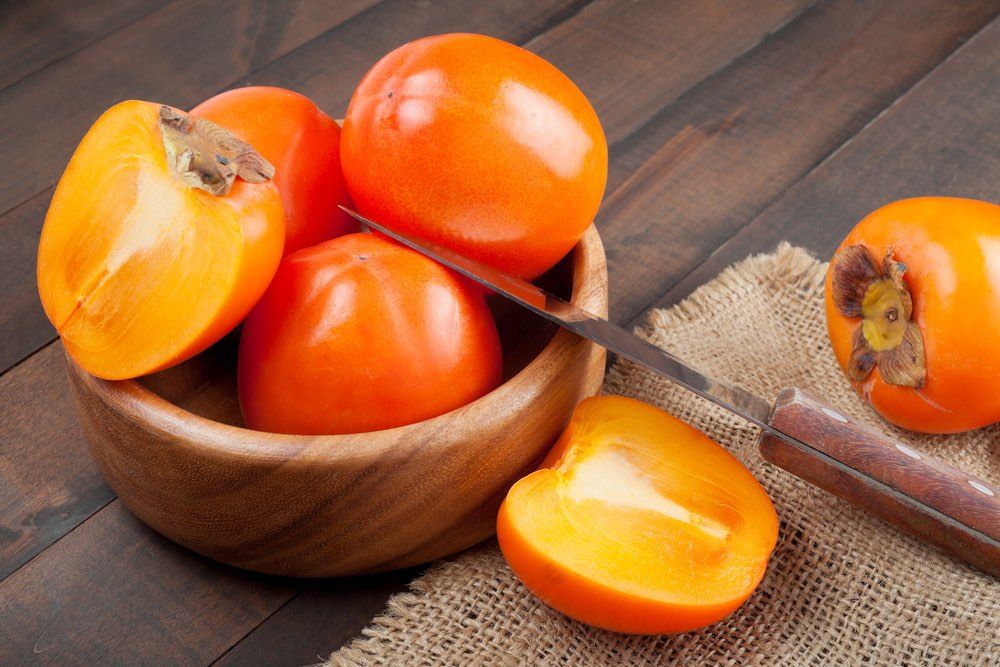 persimmons in bowl on wooden table