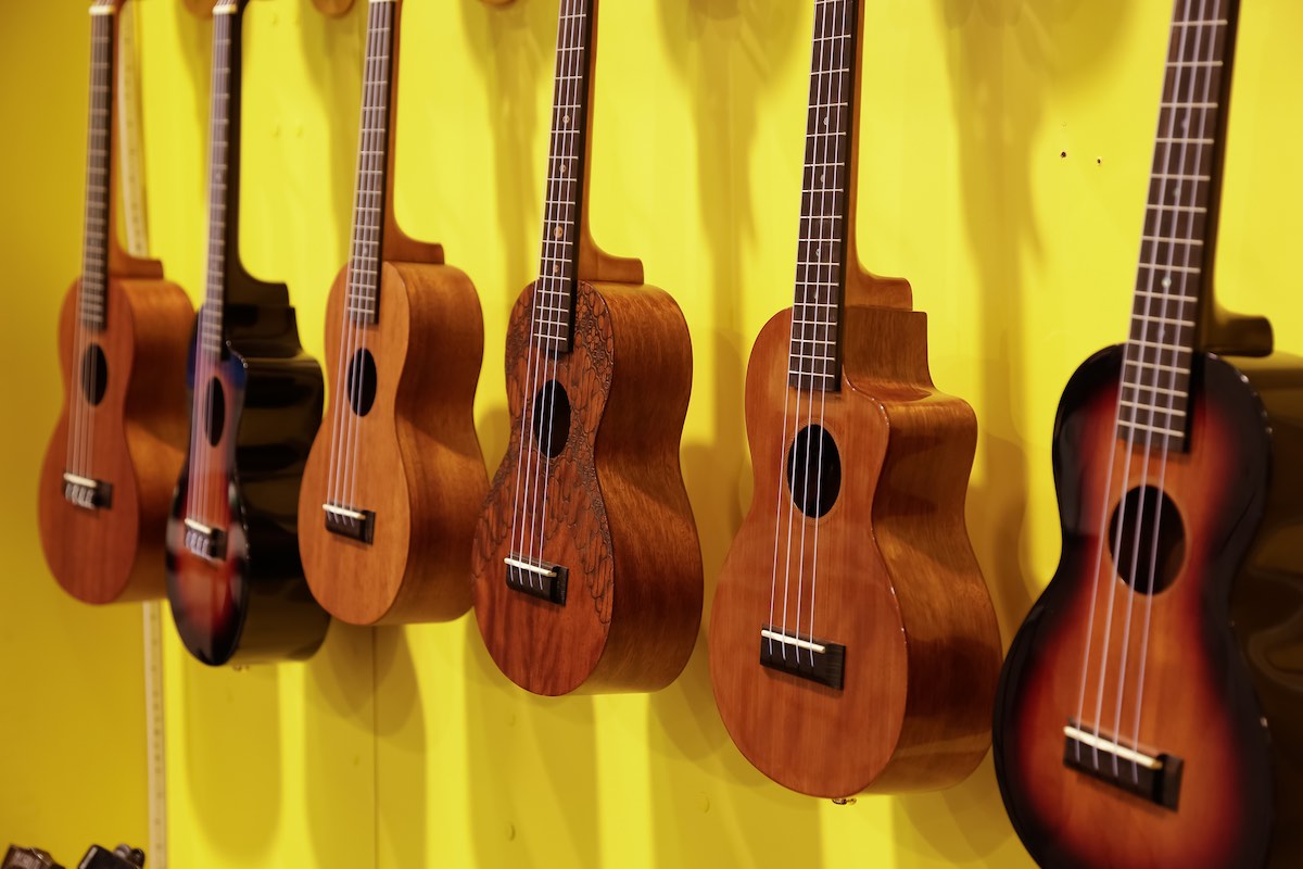 Find out which Hawaii souvenirs are worth buying according to top Hawaii blog Hawaii Travel Spot! Image of a bunch of ukuleles on a yellow wall