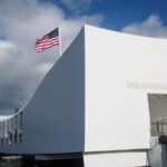 Check out how to visit Pearl Harbor on Oahu by top Hawaii blog Hawaii Travel Spot. Image of An American flag flys over the Arizona Memorial where the USS Arizona was sunk during the attack on Pearl Harbor on Oahu Hawaii.