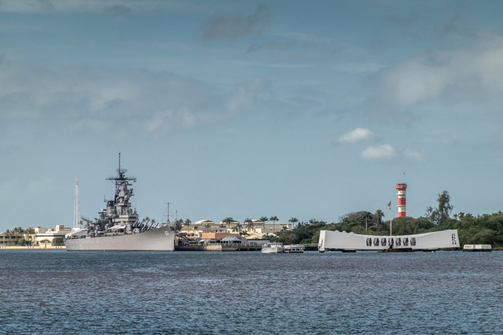 Image of Oahu, Hawaii, USA. - January 10, 2020: Pearl Harbor. Gray USS Missouri together with USS Arizona Memorial side by side on blueish water and under blue cloudscape. Airfield tower, Green foliage belt.